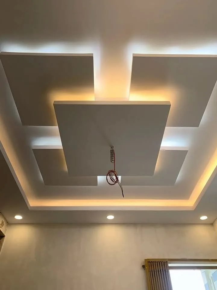 Portrait view of a floating white ceiling tray washed by warm amber cove light above a seating area.